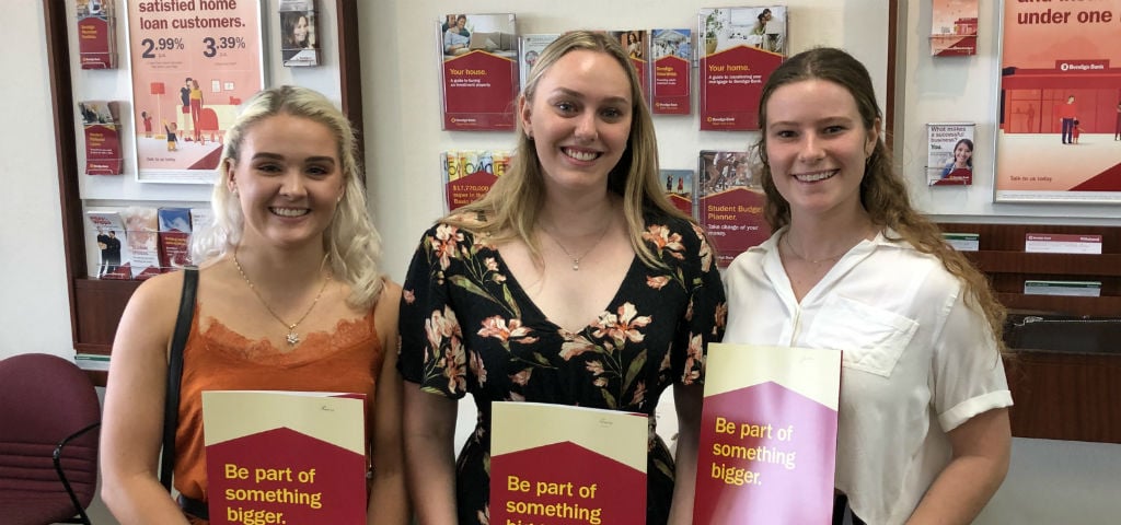 Three female scholarship winners standing in branch holding their scholarship packs.